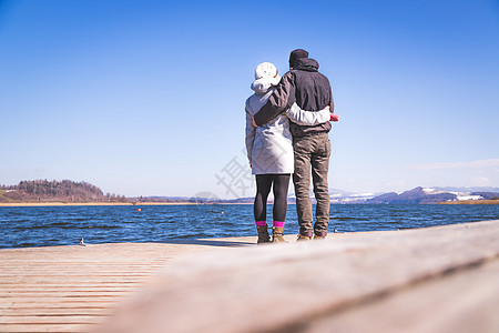 快乐的年轻夫妇正站在一个脚桥上 享受着湖边风景 冬天空闲天桥休闲装海岸女孩假期女性海洋女士晴天图片