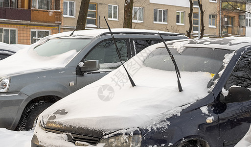 雪地上的汽车暴风雪过后的城市街道 汽车被困在冰雪之下 车辆被埋在路上的雪堆中 冬天大雪过后的停车场 未清洁的道路 破纪录的降雪量城市街道危险背景