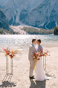 新郎在婚礼场地为新娘戴上戒指 在意大利的背景下 以秋季花柱拱形为背景 欧洲的目的地婚礼 在 Braies 湖山脉湖泊丝带森林游客图片