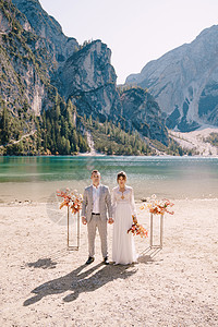 新娘和新郎在意大利的背景下 以秋花柱为拱门站立了仪式 欧洲的目的地婚礼 在Braies湖上举行树叶恋人分支机构薄纱新婚裙子游客岩图片