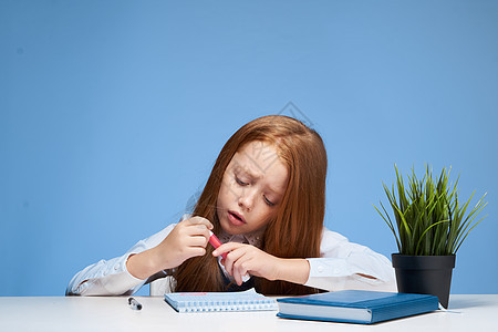 坐在学习桌旁的红头发女孩在教育中学习生活方式创造力教科书幼儿园桌子学校瞳孔女学生笔记本课堂班级图片