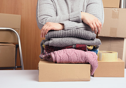 身穿灰色毛衣的妇女把衣服包装在盒子里 援助和志愿的概念 搬家图片