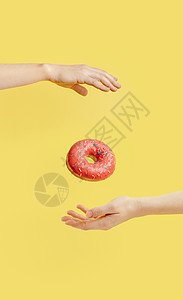 黄背景的甜甜圈落在两手之间图片