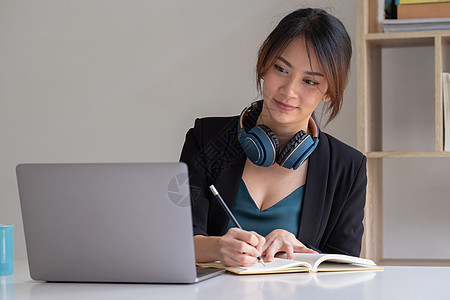 快乐的亚洲女性在办公室用笔记本工作时 在笔记本上做笔记图片