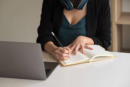 女人坐在办公桌前做笔记 同时在笔记本电脑听力学习课程会议上在线学习网络研讨会播客 电子学习概念图片