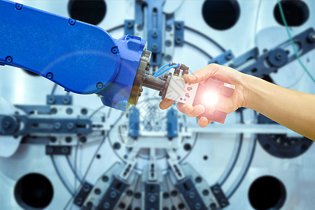 工业机器人与人的握手关系 用于在概念工业 4 0 的工业制造中使用耀斑过滤器和在蓝色调背景上工作的模糊机械图片