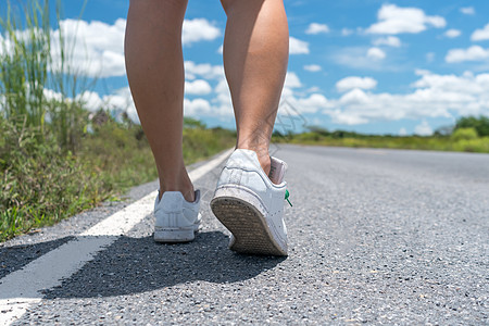 女性在乡村小路上行走 蓝天背景运动鞋生活男性鞋类旅行人行道慢跑者沥青运动装女孩图片