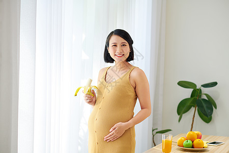 孕妇在有健康果汁和吃香蕉的起居室中婴儿休息收费食物怀孕桌子水果女士腹部女性图片