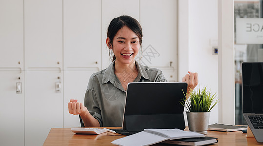 使用笔记本电脑并庆祝在线学习或在家工作的成功 对兴奋的年轻亚洲女孩进行肖像式宣传快乐企业家桌子女士职场商务技术经理人士女性图片