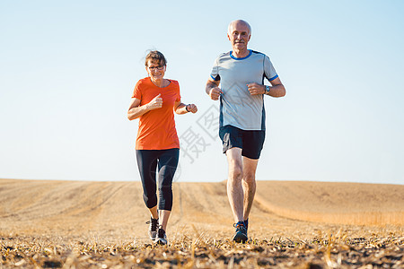 高级男女在田野上跑步或慢跑女士背光老年夫妻旧爱场地喜悦天空赛跑者男人背景图片