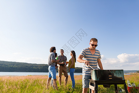 湖边烧烤在湖边做BBQ的年轻人 clique男生派对感觉团体草原友谊女孩们男孩们烤架食物背景