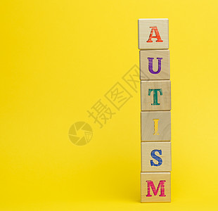黄色背景上刻有自闭症铭文的木制立方体 对大脑发育障碍儿童的支持和鼓励概念图片