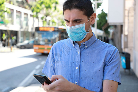 戴着外科口罩的男子用智能手机在互联网上更新有关城市交通的信息 大流行冠状病毒期间通过手机支付交通费用的在线票务服务图片
