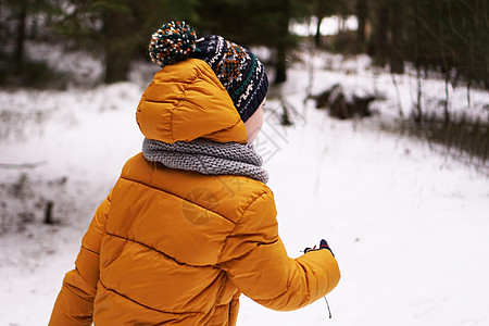 一个穿着黄黄色夹克的小孩 和一只帽子在冬天走在森林里图片