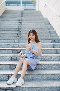 坐在室外楼梯和使用智能手机的美丽的年轻亚裔妇女 现代女性的生活方式微笑街道城市潮人女孩互联网电话闲暇咖啡杯子图片