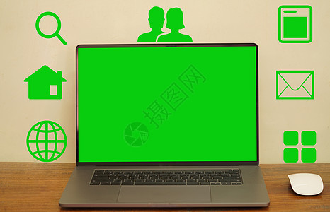 一个抽象的绿色屏幕笔记本电脑和鼠标放置在一张长桌上 图标上显示符号以利用各种程序图片