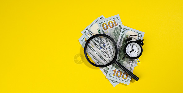 寻找收入 利润和时间较少的利润的概念 在黄背景上使用一个放大玻璃来遮盖美钞100美元纸币和放大镜背景图片