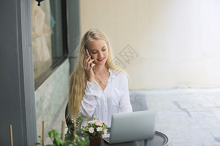 美丽的金发女郎在手机上讲话 笔记本电脑放在咖啡店外的桌子上工作技术女士商业工具互联网人士说话商务女性图片
