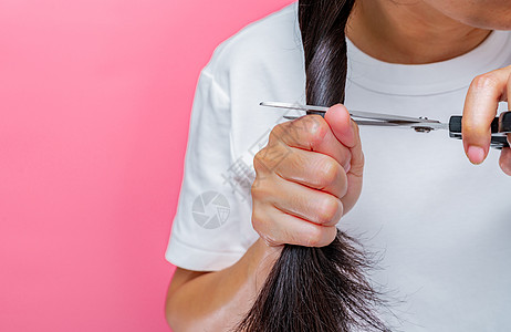 女性剪掉受损和干燥的头发 亚洲妇女用剪刀剪头发以捐赠给癌症患者 为乳腺癌患者捐赠头发 粉红色背景中留着黑色长发的女人图片