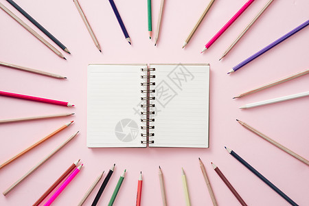 中间的笔记本上印着亮色铅笔 贴在粉红色背景周围图片