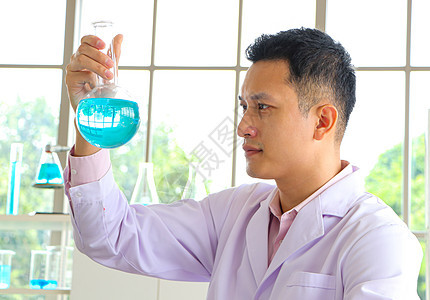 一位亚洲科学家或化学家在实验室里看着蓝色液体化学试管生物样本显微镜化学品器皿药品工作玻璃医院微生物学图片