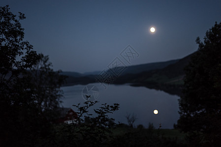 午夜时分 月光从满月闪耀的月光照耀在湖中 周围有山林和树木图片