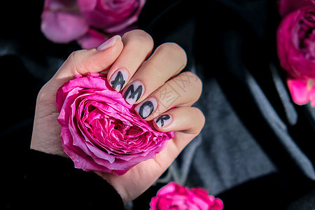 指甲修指甲上的 AMOR 字样在黑色丝绸织物上挂着粉红色的玫瑰花 最小的平躺自然 女手 爱表皮设计女性艺术化妆品护理玫瑰温泉凝胶图片