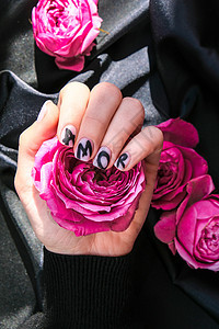 指甲修指甲上的 AMOR 字样在黑色丝绸织物上挂着粉红色的玫瑰花 最小的平躺自然 女手 爱化妆品女士沙龙爱情艺术凝胶皮肤设计美甲图片