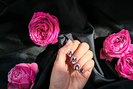 指甲修指甲上的 AMOR 字样在黑色丝绸织物上挂着粉红色的玫瑰花 最小的平躺自然 女手 爱表皮设计温泉沙龙艺术抛光女性护理指甲油图片