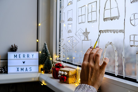 女手在窗户玻璃上画圣诞假期装饰 新年风景 城市建筑花环灯 Hygge 装饰和圣诞节概念庆典女士绘画假期反思雪片传统地标女性展示图片