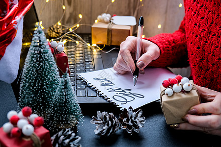 一张纸 上面有文字礼物清单 上面有圣诞装饰品 戴着圣诞老人的帽子 假期网上购物 冬盐桌子笔记本工作电脑盒子女士写作办公室职场礼品图片