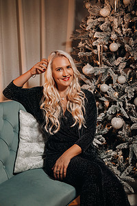 一个穿着晚礼服的女孩坐在 圣诞树附近的沙发上幸福女性化喜悦头发红色假期新年乐趣女士裙子图片