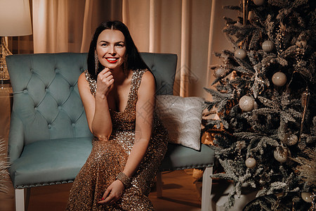一个穿着晚礼服的女孩坐在 圣诞树附近的沙发上女性化红色女士裙子幸福头发奢华假期乐趣新年图片