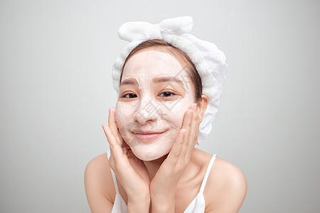 女人在白色背景 干净的脸霜 在脸上毛巾上脸部毛发头部皮肤成人温泉沙龙护理黏土女士化妆品洁净治疗图片
