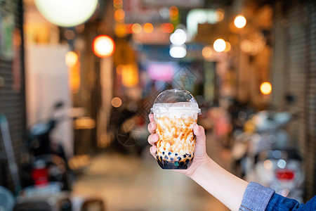 年轻女孩在台湾背景的夜市里 拿着并展示一杯咖啡棕色糖味木薯珍珠泡泡奶茶 闭紧了 bokeh旅行街道游客老虎泡沫条纹美味美食牛奶波图片