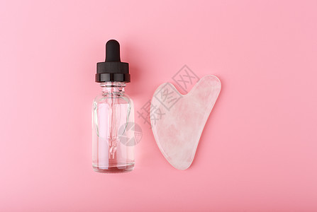 透明瓶中的按摩凝胶 血清或油以及粉红色背景中的心形瓜沙粉石英晶体护理商品美容技术叶子宝石工具面部福利皱纹图片