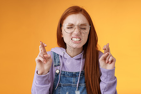 女孩渴望胜利 心底恳求 认真咬牙 皱眉 闭眼 祈求主 十指祈求 好运 许愿 站着 橙色背景 梦想成真欢呼学生头发工作室幸福女朋友图片