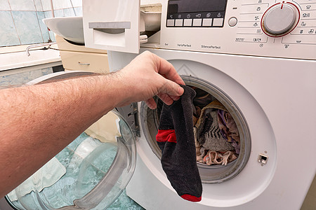 洗衣机内部一只手握着干净的黑袜子 在露天洗衣机前背景