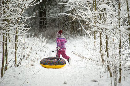 一个冬天的小女孩 穿着紫色衣服和一个充气圈 在一片雪覆盖的森林里走在街上童年女孩季节雪花孩子圆圈骑术街道孩子们微笑图片