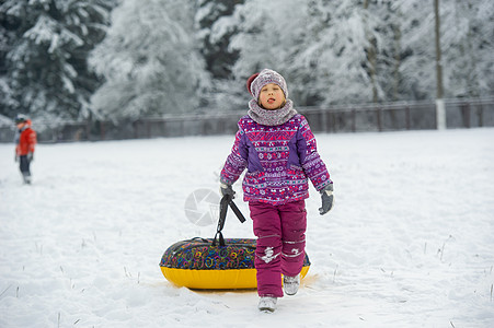 一个冬天的小女孩 穿着紫色衣服和一个充气圈 在一片雪覆盖的森林里走在街上季节圆圈森林圣诞礼物游戏童年帽子手套微笑骑术图片