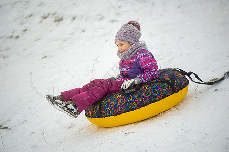 一个冬天的小女孩 穿着紫色衣服和一个充气圆圈 在街上的山下骑马孩子们小姑娘新年手套雪花帽子游戏微笑童年设施图片