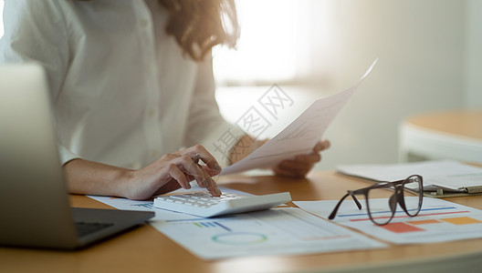 女商务人士或会计师工作财务经理研究过程会计计算与计算器分析市场图表数据库存信息审查在办公室的桌子上图片