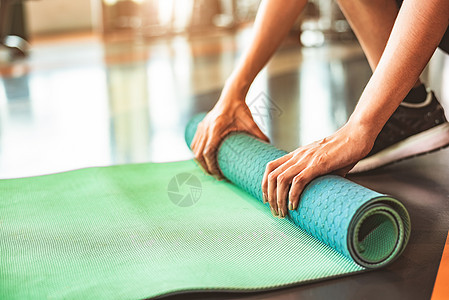 在运动健身健身房训练中心背景下特写运动型女性折叠瑜伽床垫 瑜伽课后保持运动垫滚动 锻炼和运动训练概念 手放在地毯上运动装冷却体操图片