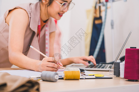 在家庭办公室车间工作的迷人亚洲女性时装设计师 时尚的时尚达人女性创造新的布料设计系列 裁缝和缝纫 人们的生活方式和职业概念工作室图片