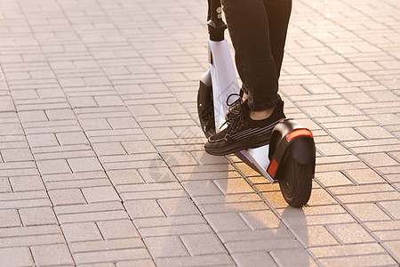 穿着黑色运动鞋的腿男骑着电动移动滑板车 现代人在阳光明媚的日子里使用电动滑板车 成年男子骑电动滑板车上班 环保交通图片