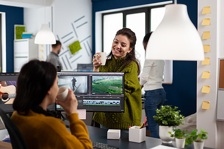 在工作间休息期间喝咖啡和聊天的摄影师坐在办公桌旁剪辑艺术家办公室监视器公司机构设计师镜头展示团队图片