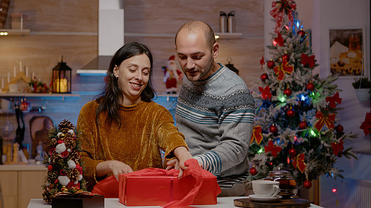 男人和女人在圣诞节礼物上包装红色纸的红皮季节假期已婚毛衣微笑家庭厨房丝带享受新年图片