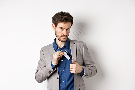 自信而成功的商务人士看起来自信 同时把塑料信用卡放在西装口袋里 站在白色背景上促销购物商务套装胡须男性工人企业家工作快乐图片