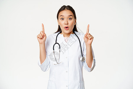 惊讶的亚洲女医生的画像 医生竖起手指 展示惊人的新闻 大促销 白色背景女孩隔离商业情况肺炎诊所专家保健实习生广告背景图片