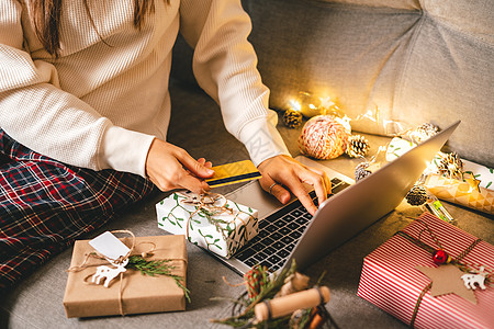 特写有信用卡 礼物和膝上型计算机的妇女手 圣诞节假期在线购物 裁剪女性坐在沙发上 配有天然生态礼物和装饰 圣诞快乐包装概念图片